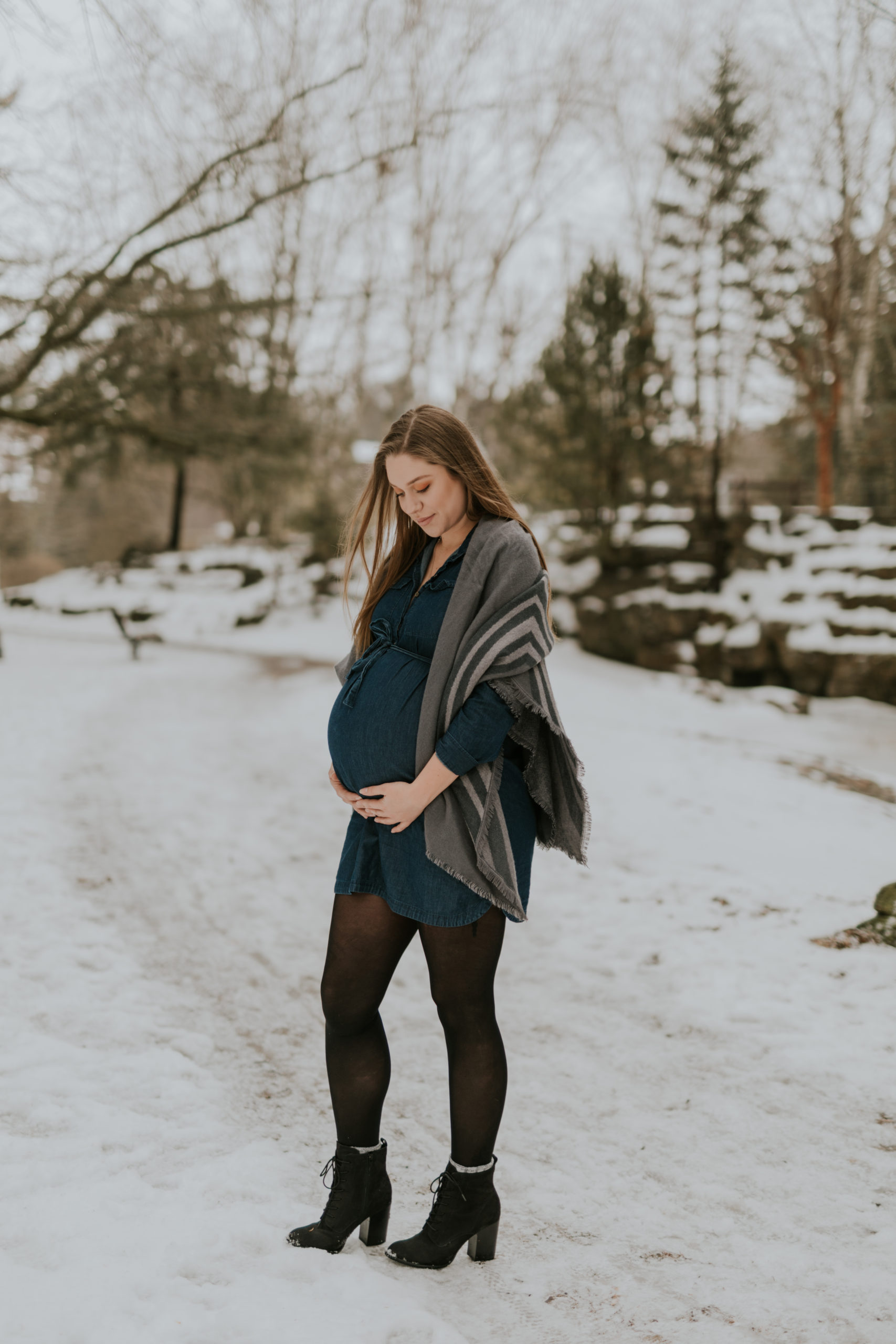 A new mom poses with her baby bump during a winter maternity session with Cara Gilhula Photography in Stratford, Ontario at Upper Queens Park