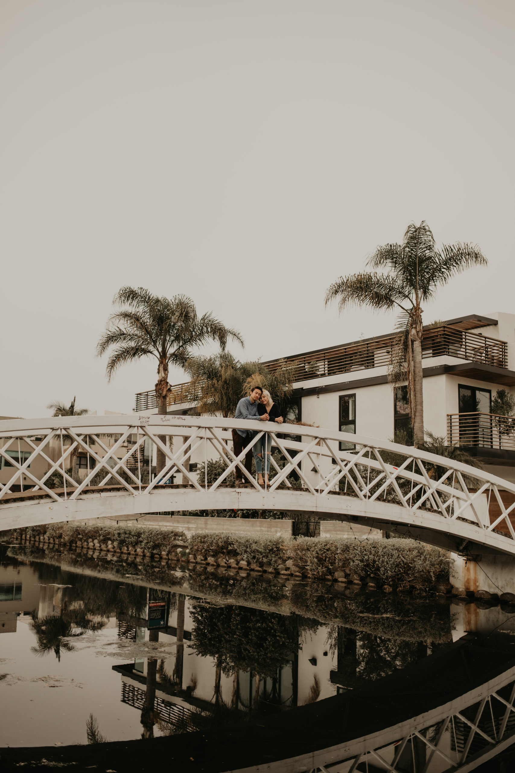 Couple cuddles during couple session on bridge with Cara Gilhula Photography at Venice Canals, California