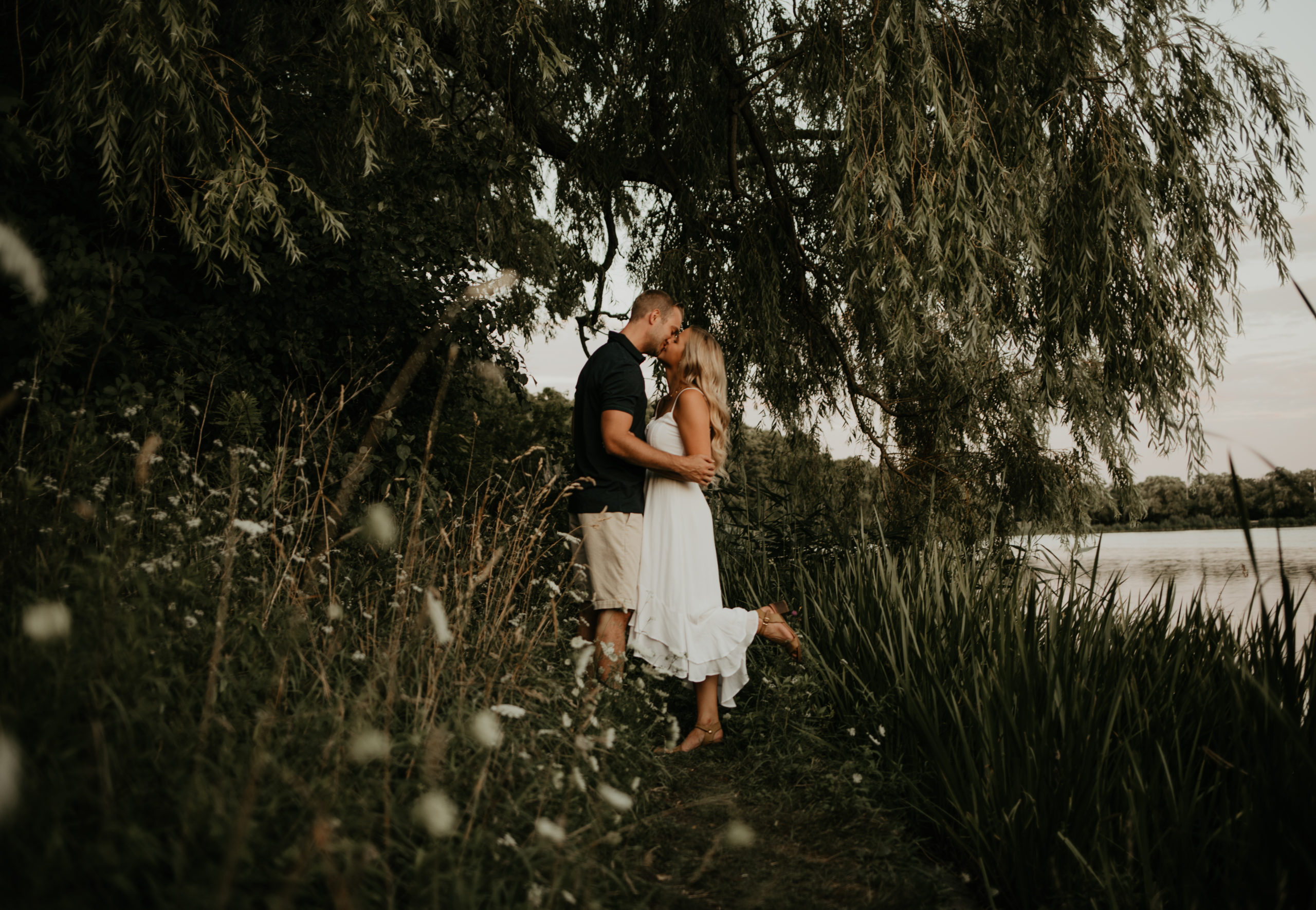 Couple share a kiss under a willow tree in High Park, Toronto during a session with Cara Gilhula Photography
