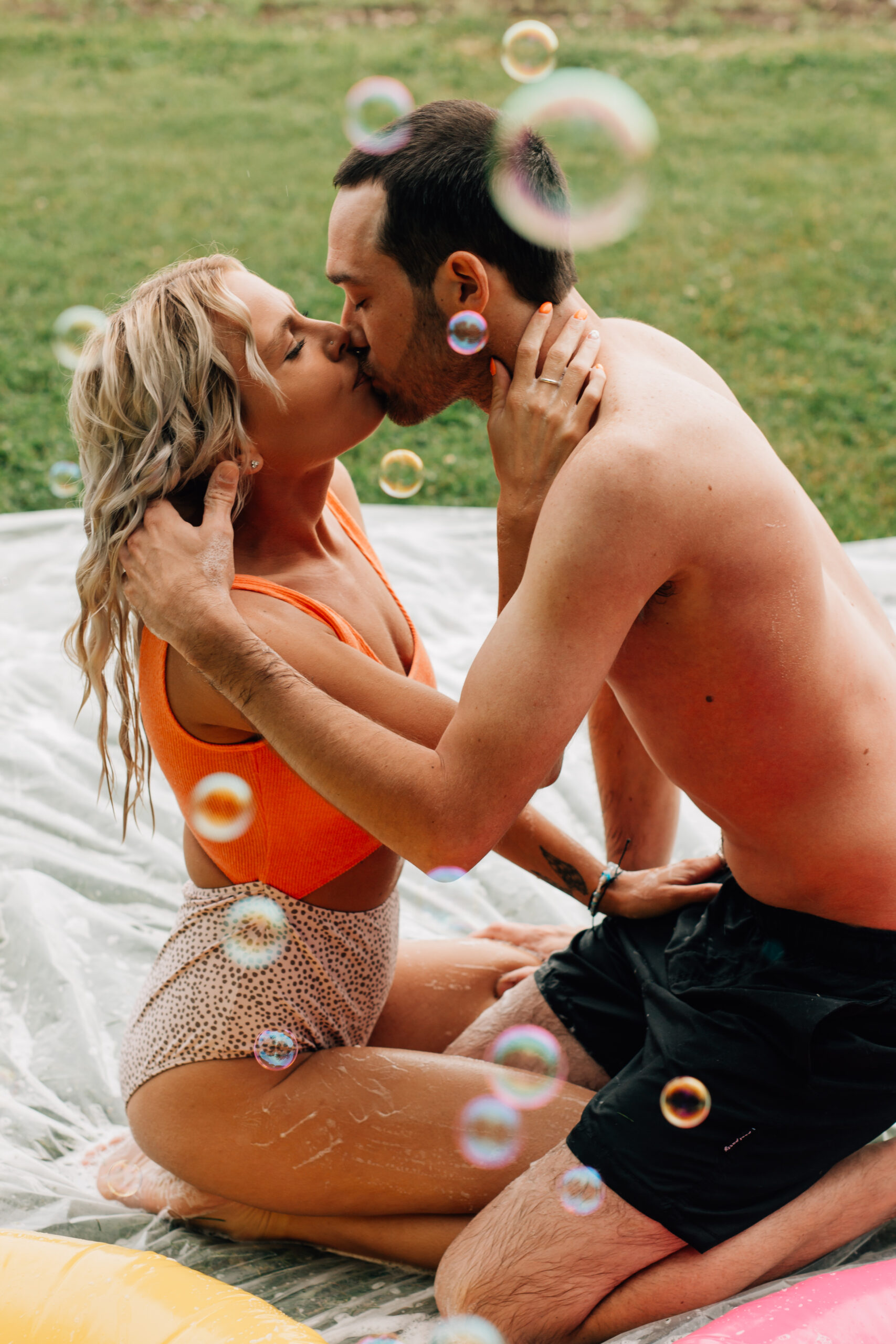 Couple share a kiss on a summer slip and slide during a photo session with Cara Gilhula Photography